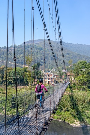 Mountain biking in Nepal. Young woman with group of mountain bikers crossing suspension bridge near Kathmandu, Nepalの写真素材