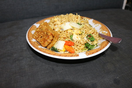 Noodles with vegetables and fried tofu on a white plate.の写真素材
