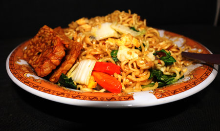 Fried mie (mie goreng) with vegetables and spices on a black background. top view. Delicious Indonesian Food.の写真素材