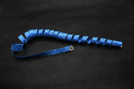 A portrait of a cloth or clothing measuring instrument, in blue with a black background. Measuring...