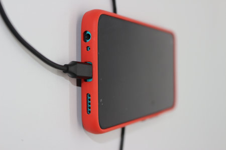 Black mobile phone being charged with red coverの写真素材