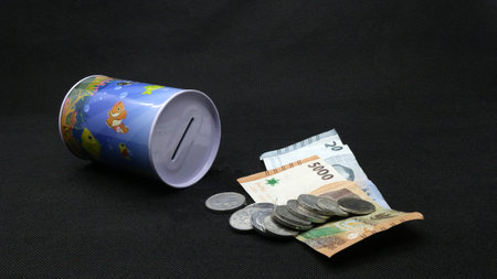 Piggy bank with scattered coins and bills on black background