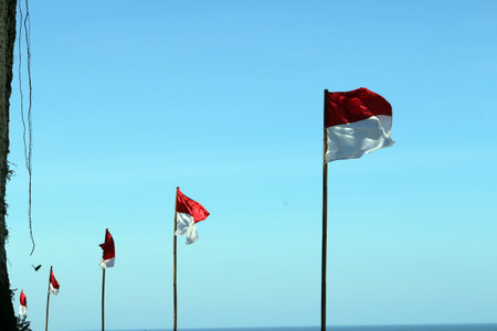 The Indonesian flag flies on a cliff with a backdrop of the beach and clear sky