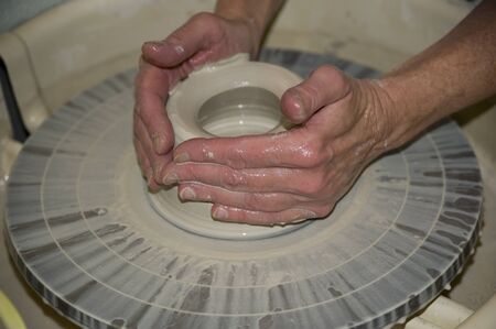 A talented potter supports new walls built of a pot on a potter's wheel.  She supports the exterior...
