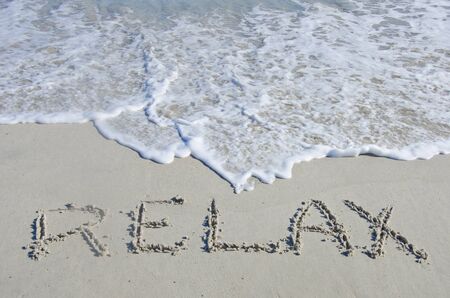 The surf of the ocean threatens to wipe away the word "Relax," written in the sand with whitewater lapping on the beach.  There is plenty of copy space available for your own message.の写真素材
