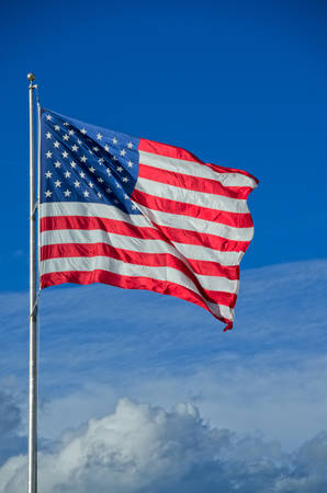 A very large American flag flies above the clouds on a beauty sunny afternoon.
