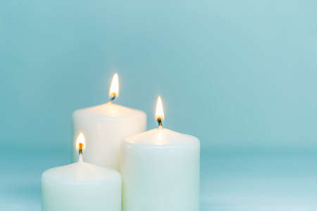 Three white candles burning on white gradient background. Front view. Horizontal composition. Set of white candles over blue background with copy spaceの写真素材