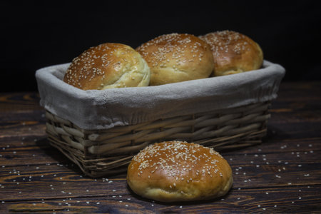 Homemade buns with sesame seeds in basket on wooden background
