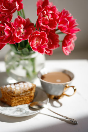 Cup of coffee with cake and red tulips on white tableの写真素材