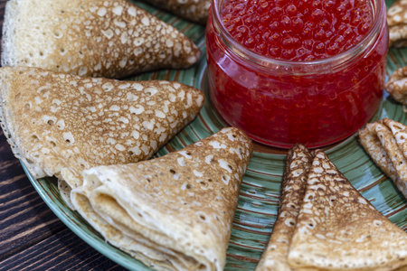 Pancakes with red caviar in a glass jar on a wooden backgroundの写真素材