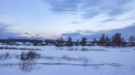 beautiful winter landscape with snow-covered field and village at sunsetの写真素材