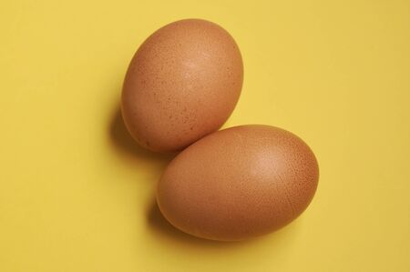 two yellow chicken eggs on a yellow background