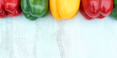 Fresh bell peppers in a row at the top of the image. White wood background. Copy space. A barber or a banner for creative ideas. Red yellow and green bell peppers. The concept of a healthy diet and fresh vegetablesの写真素材