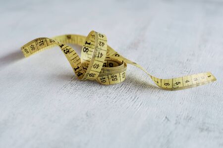 Yellow measuring tape in centimeters, curled. Measuring tape on a wooden table close-up