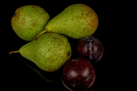 Fresh and wet pears and plums on a black background. Water drops on fruits.の写真素材