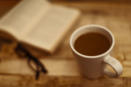 Mug cup of coffee, reading glasses eyeglass and book on a wooden table in a relaxing sceneryの写真素材