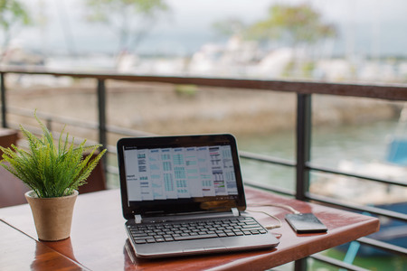 Laptop on wooden table at the yacht club cafe with online business tethering via WiFi hotspot