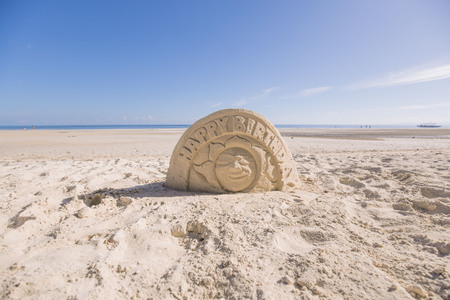 beach artist has modeling an artistic happy birthday sculpture out of sand at a white beach a summer vacation sceneの写真素材