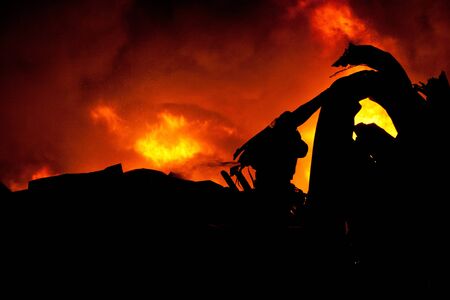 Silhouette of Firemen fighting a raging fire with huge flames of burning timber