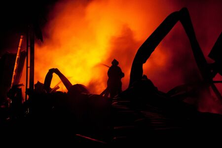 Silhouette of Firemen fighting a raging fire with huge flames of burning timber