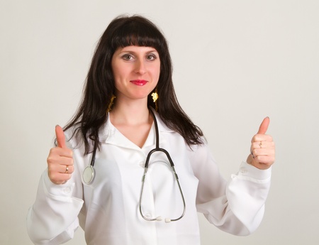 Happy smiling cheerful female doctor with thumbs up gesture, over grey backgroundの写真素材