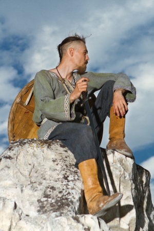 Man sitting on a rock with a sword against blue cloudy skyの写真素材