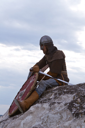 Knight sitting on a rock with a sword against blue cloudy skyの写真素材