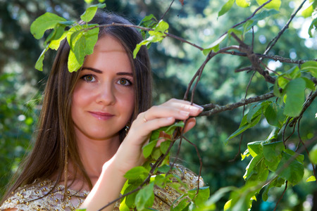 beautiful young girl with brown hair in a bright dress is walking in a summer parkの写真素材