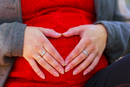 Pretty pregnant woman in red posing in green park. Young woman holding her tummyの写真素材