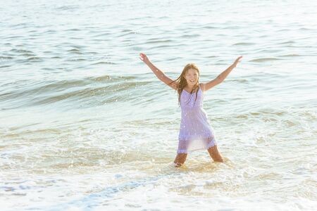 beautiful blonde teenage girl wearing flowy white dress standing ankle dee in ocean waterの写真素材