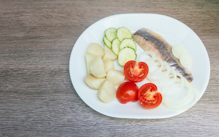 herring salad with vegetables on white plate top view potato onion tomato herringの写真素材