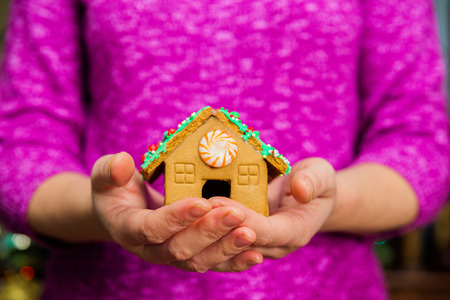 Female hands holding little gingerbread house on table with Christmas decorations.の写真素材