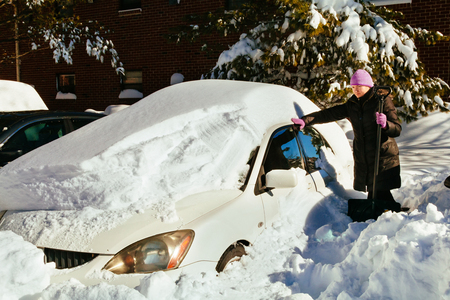 Beautiful young woman removing snow from her car beautiful woman cleans snow on carの写真素材