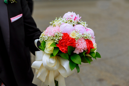 The groom holds a bouquet of white and pink flowers with male handsの写真素材