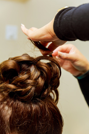 Woman hairdresser making hairstyle using curling iron for long hair of young female with smartphone in beauty salonの写真素材