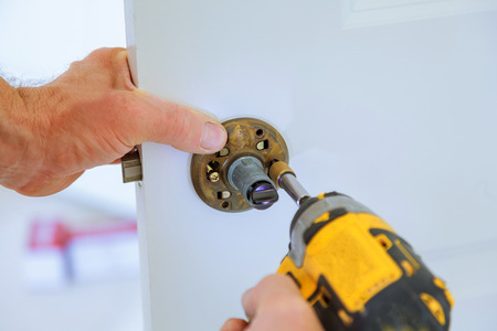 carpenter at lock installation with electric drill into interior wood door