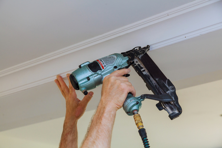 Carpenter brad using nail gun to Crown Moulding framing trim, with the warning label that all power tools have on them shown illustrating safety conceptの写真素材