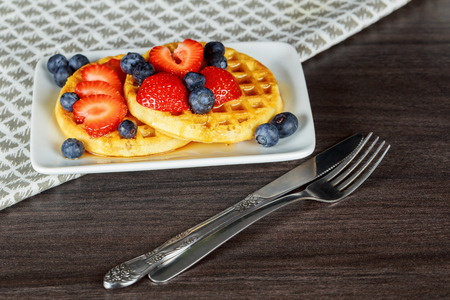 Healthy breakfast: Belgian waffles with sour cream, strawberry, raspberry, blueberry, cherry and red currant on blue wooden table. Selective focusの写真素材