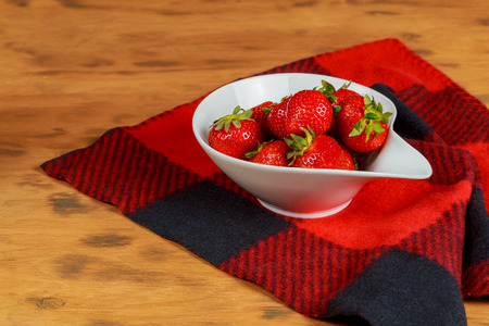 Ripe red strawberries on wooden table in a simple white bowlの写真素材