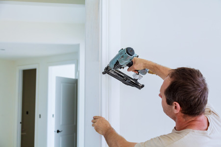 Carpenter brad using nail gun to moldings on doors, all power tools have on them shown illustrating...