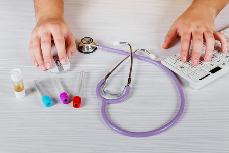 Close up of unknown female doctor sitting at the table near the window in hospital and typing at laptop computerの写真素材