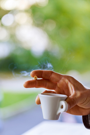 close up man's hand with a cup of black coffee and a cigaretteの写真素材