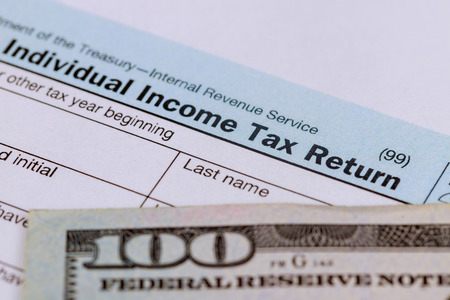 Tax time - Closeup of U.S. 1040 tax return with 100 bills pay taxの写真素材