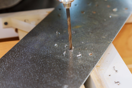 Electric drilling machine with manual pressure, a man holding a metal part and the hole is drilled,...