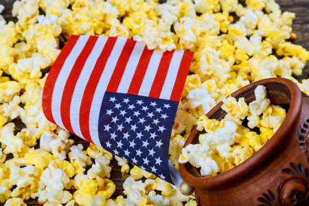 Salty popcorn in a wooden cup is on a white table. American flag flying, flag USA Popcorn lies...