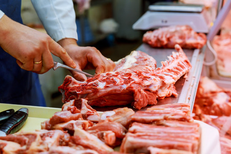 Cropped image of male butcher cutting raw meat with knife at counter in shopの写真素材