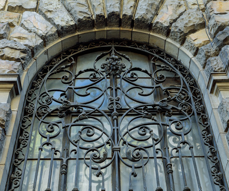 An ancient wrought-iron grille, a decorative security element. An old grille on the window of an old house with beautiful brick wall paintings. Classical metal forged cage. Colorful brick wallの写真素材