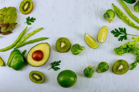 Green vegetables and herbs assortment around wooden cooking board on a white background. Fresh organic produce. Healthy food. Top view, copy spaceの写真素材