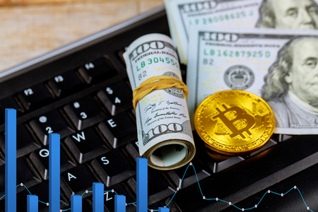 Golden dogecoin cryptocurrency coin Gold Bitcoin lying on a pile of US dollar cash banknotes, next to a black PC computer keyboardの写真素材
