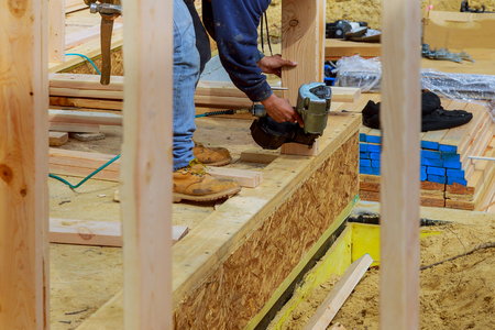 Building contractor worker with a air nail gun nailer working on the corner of first floor walls on a new home constructiion project.の写真素材